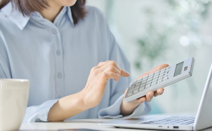 電卓を手にノートPCでコスト計算を行う担当者、アパレルECの撮影費削減を検討するイメージ